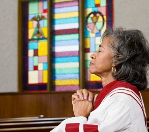 A woman in white shirt and red sash praying.