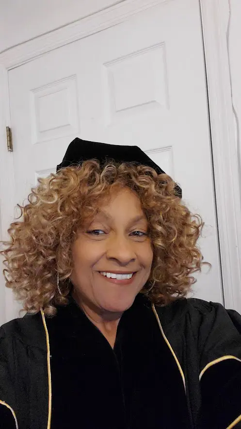 A woman with curly hair wearing a cap and black gown.