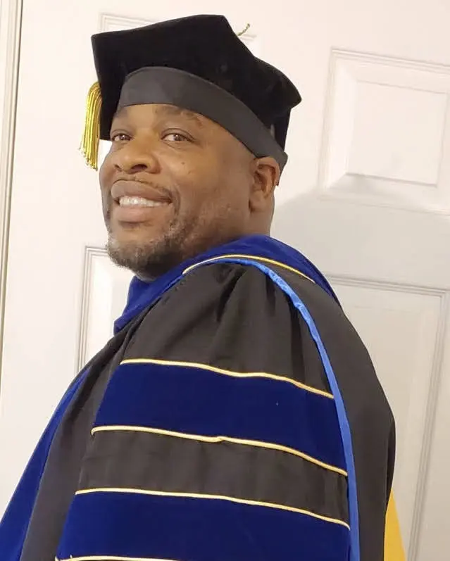 A man in graduation gown and cap smiling.