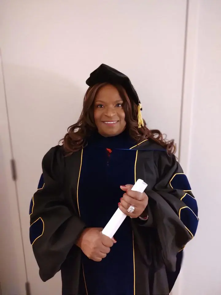 A woman in graduation gown holding a white pen.