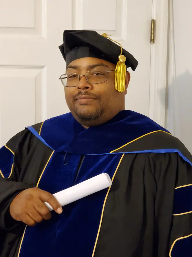 A man in graduation robes holding a white diploma.