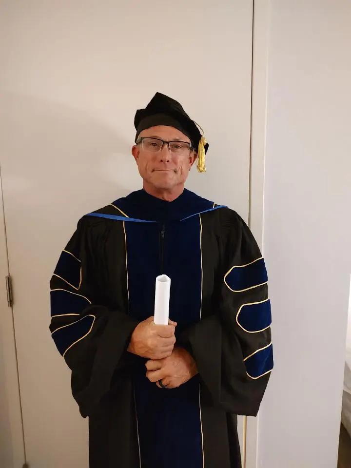 A man in graduation robes holding a white diploma.