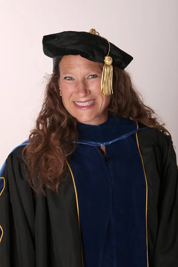 A woman in graduation gown and cap smiling for the camera.