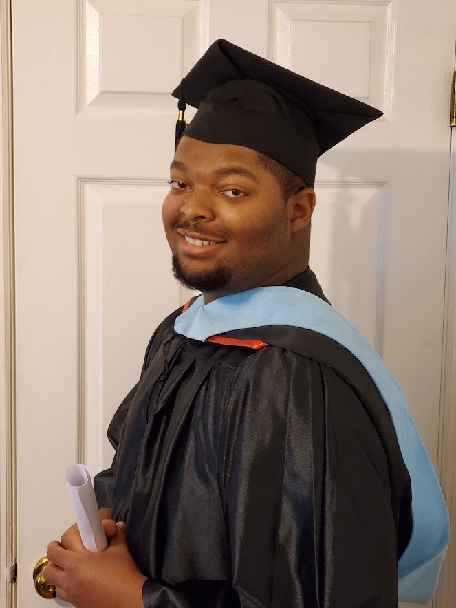 A man in graduation gown holding a pen.