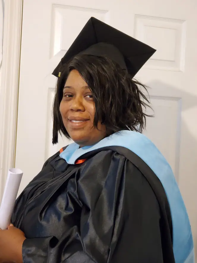 A woman in graduation gown holding her diploma.