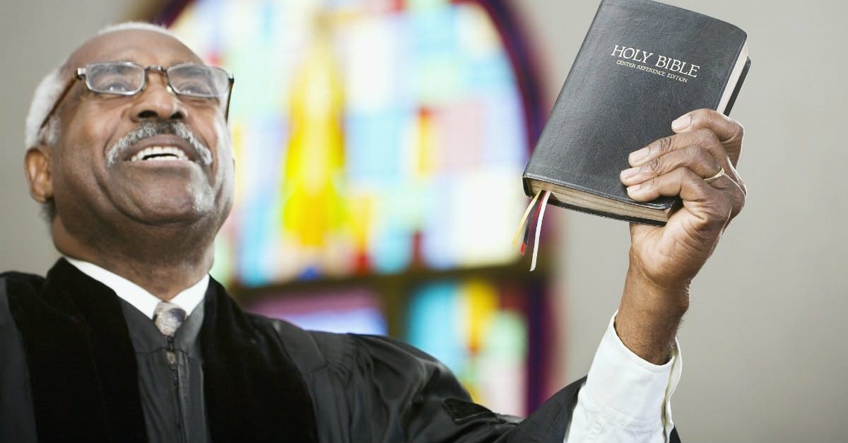 A man holding up a bible in front of stained glass.