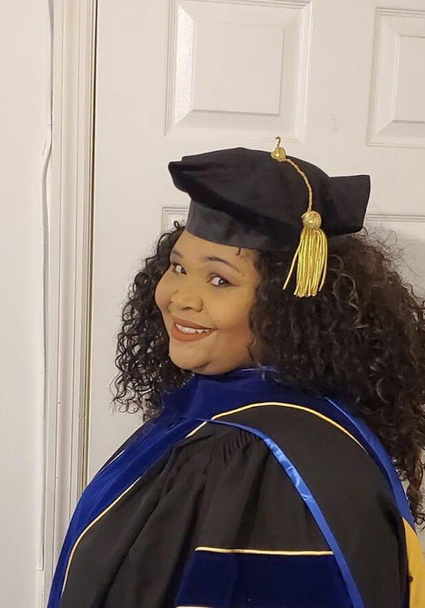 A woman in graduation gown and cap standing next to door.